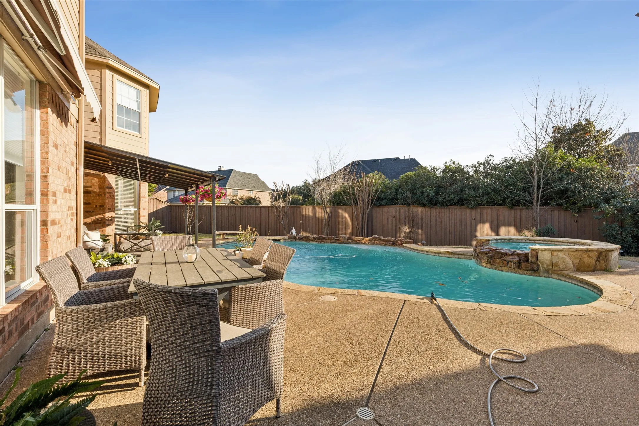 Brick exterior with a covered patio, freeform swimming pool, and raised spa with stone coping