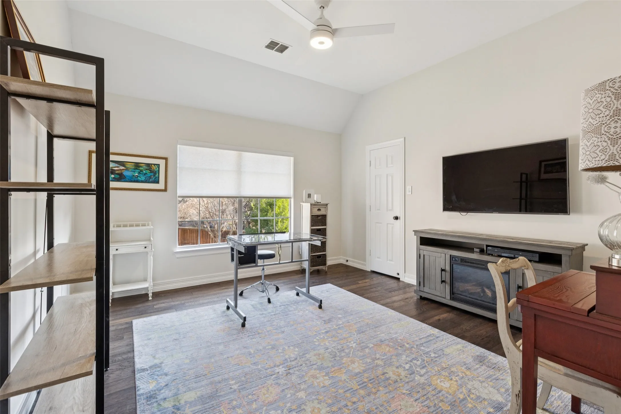Vaulted ceilings enhance this room featuring dark wood-finish flooring, a contemporary ceiling fan, and a large window with a roller shade