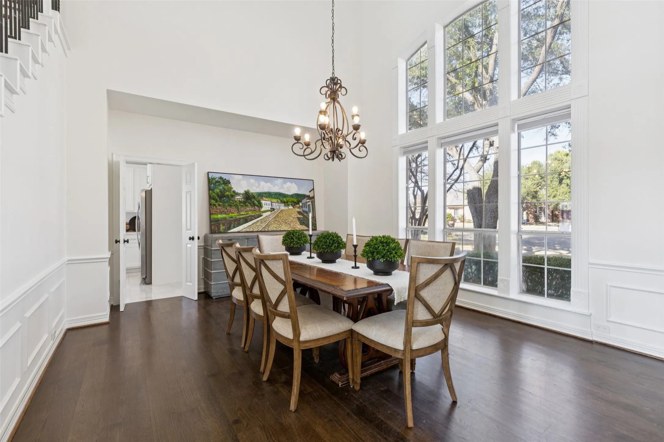 Dining space featuring soaring ceilings, expansive two-story windows, dark wood-finish flooring, wainscoting, and a wrought iron chandelier