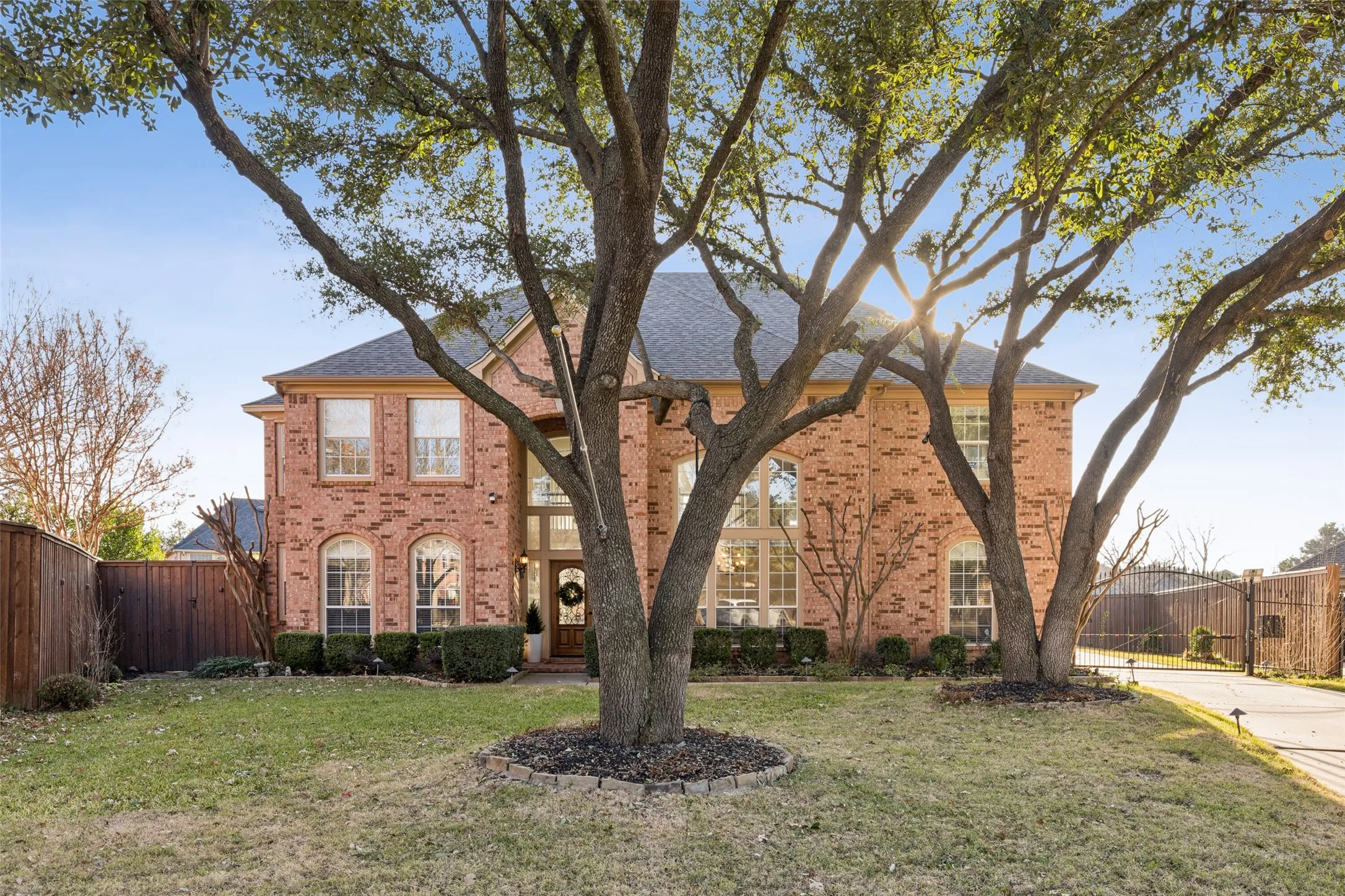 Traditional brick residence featuring a prominent gabled roofline, multiple arched windows, a grand double-height entry, and a paved driveway accessed through a gated entrance