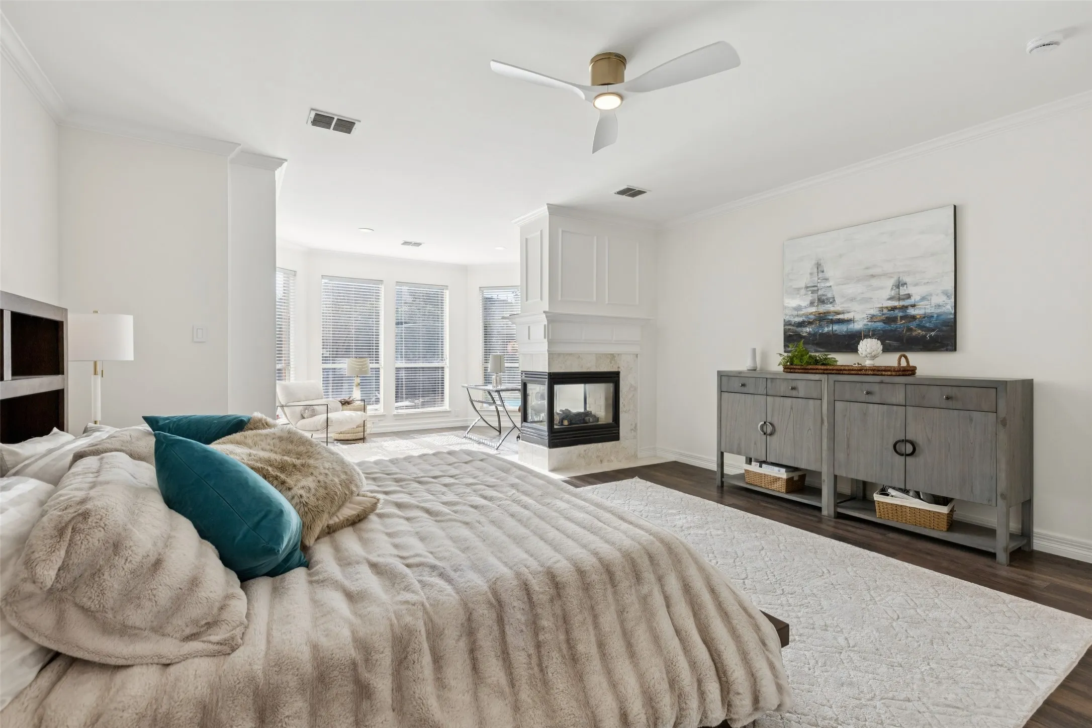 Spacious bedroom featuring dark wood-finish flooring, a contemporary ceiling fan, and a built-in fireplace with a stone surround