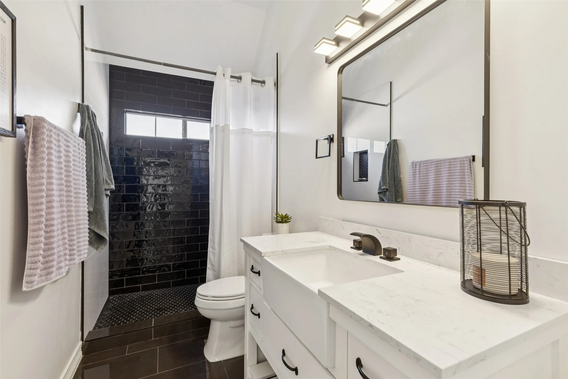 Bathroom featuring a white shaker-style vanity with a farmhouse sink, white countertop, and dark-bronze hardware