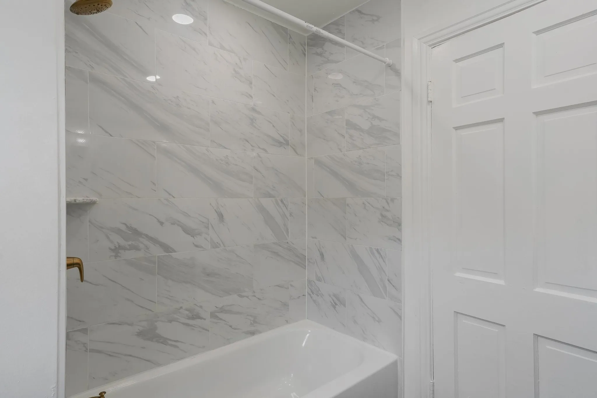 Bathtub with marble-look tile surround, recessed lighting, and gold rainfall shower head