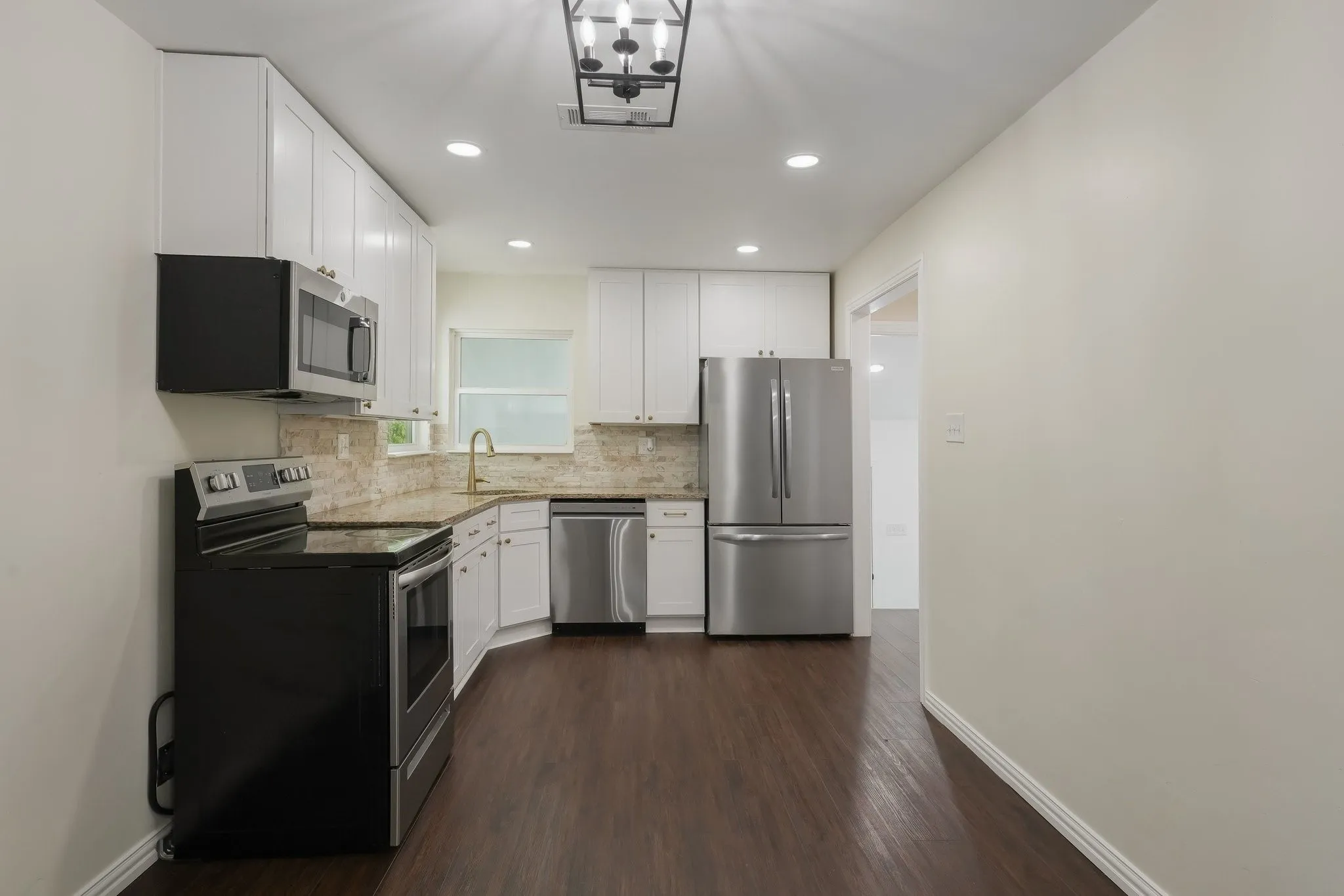 Modern kitchen featuring white cabinetry, stainless steel appliances, granite countertops, gold fixtures.