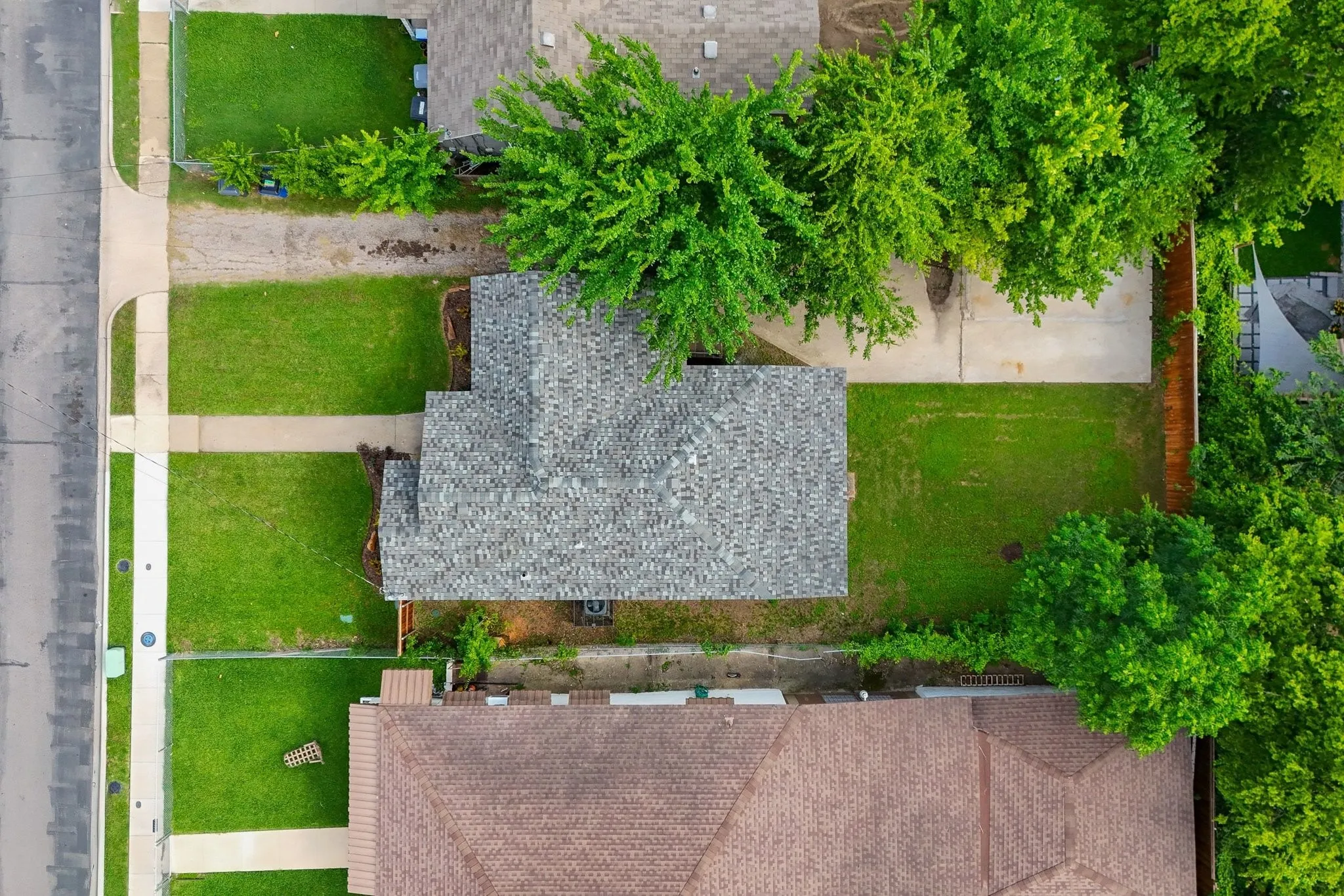 Aerial perspective showcasing a property with a gray shingle roof, a front lawn, and a concrete driveway