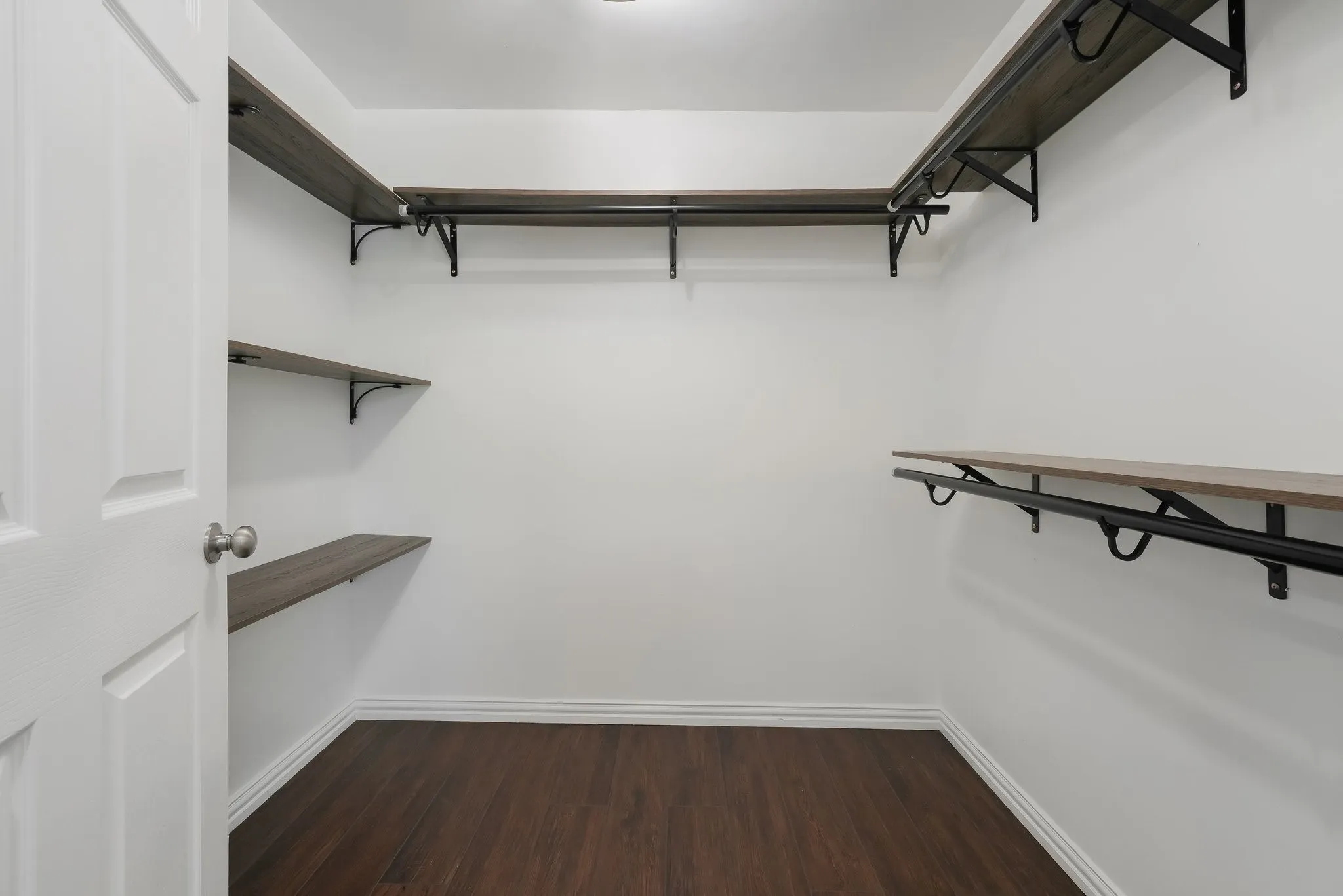 Spacious walk-in closet featuring white walls, and built-in shelving with hanging rods