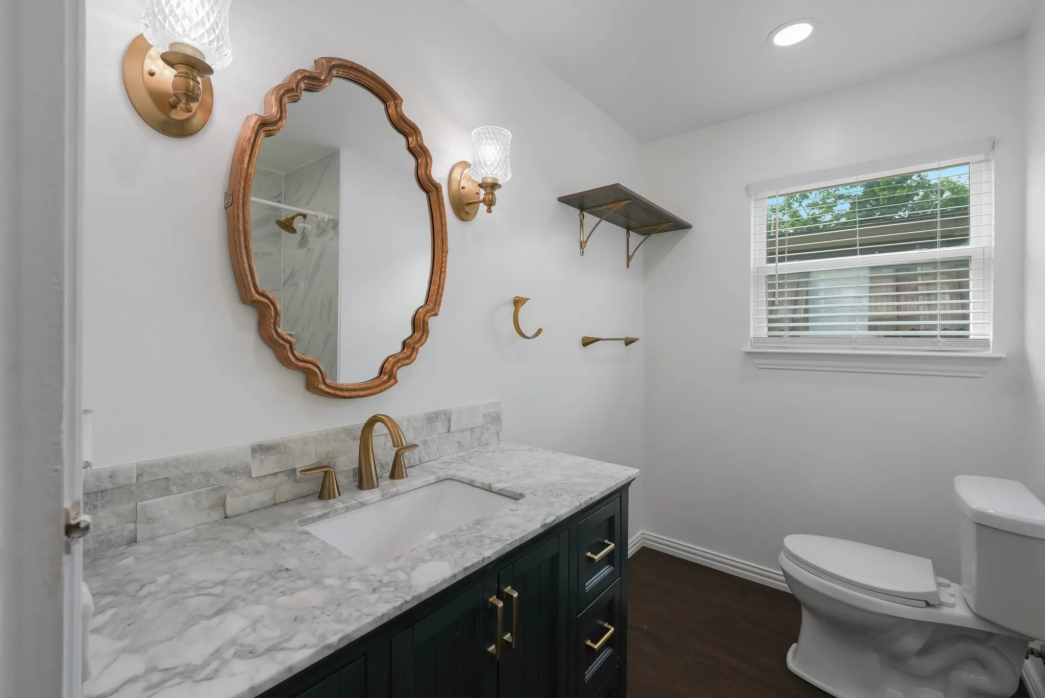 Bathroom featuring a vanity with a light-toned countertop, a decorative mirror, and wall-mounted sconces.