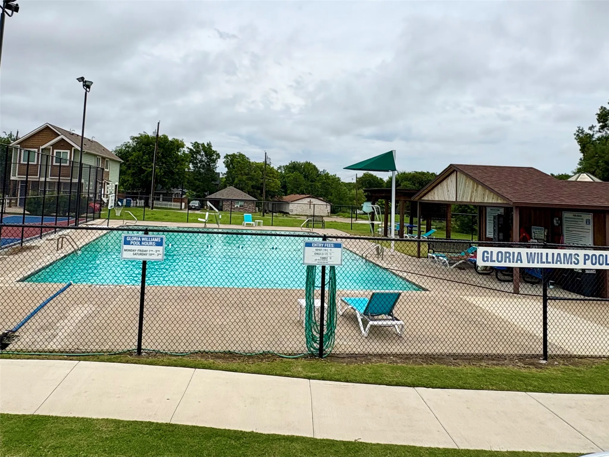 Community swimming pool with surrounding concrete decking, a pool house, and an adjacent tennis court