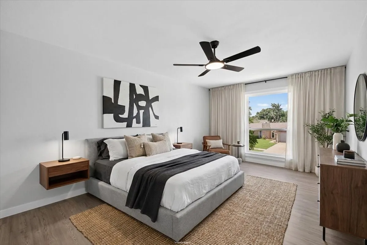 Virtually staged Spacious room featuring wood-finish flooring, a large window with privacy drapes, and a contemporary ceiling fan with integrated lighting