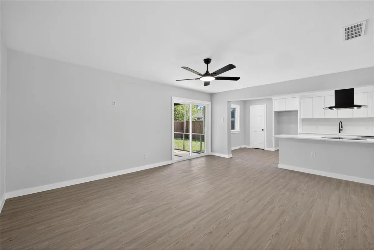 Open-concept living area with wood-finish flooring, white baseboards, and a black ceiling fan