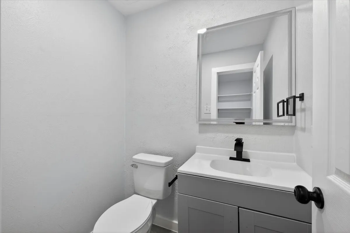 Bathroom featuring a white toilet, gray vanity with white countertop, integrated sink, and matte black faucet