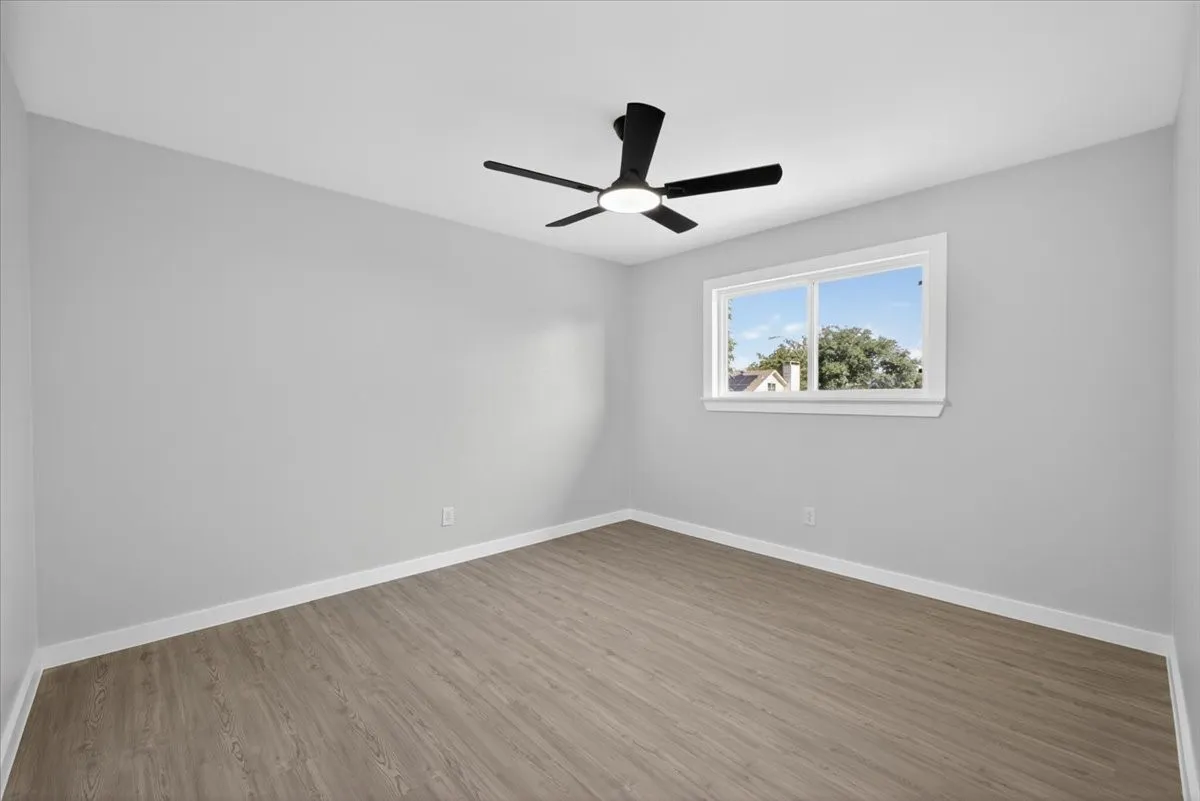 Room with light gray walls, wood-finish flooring, a modern black ceiling fan with integrated lighting, and a white-framed window