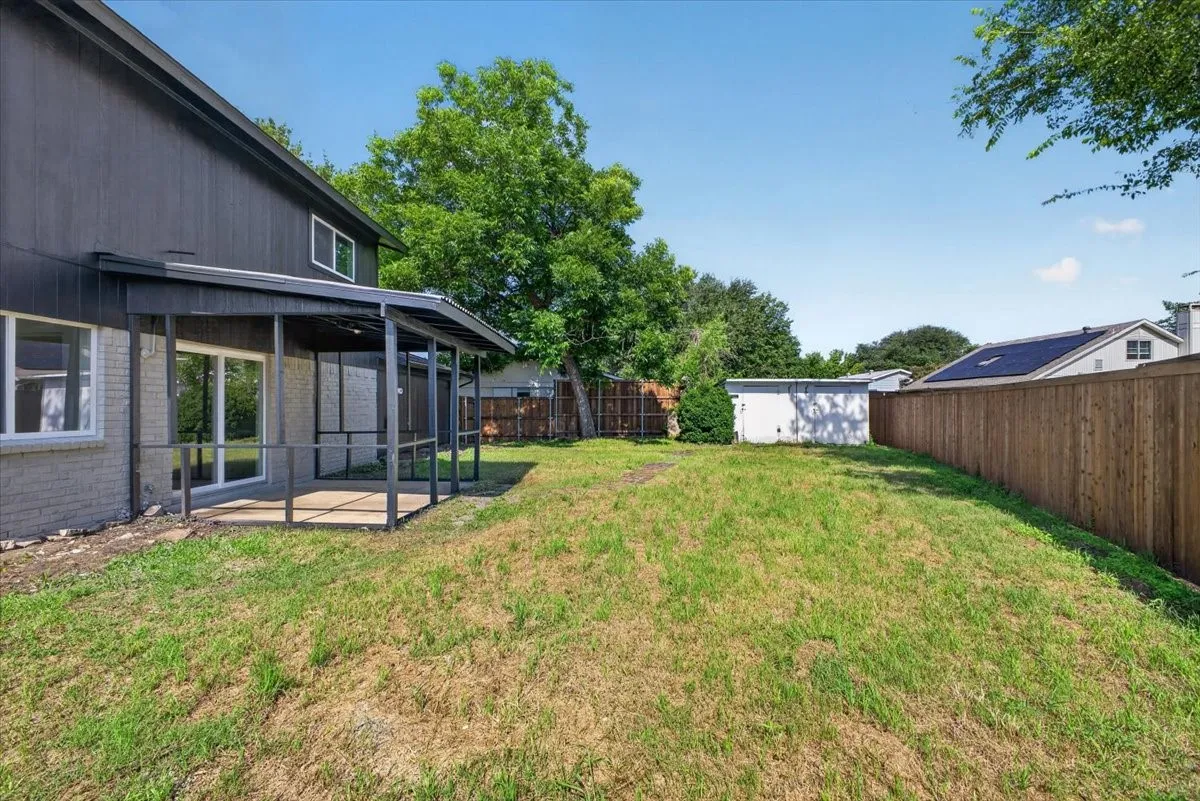 Expansive backyard featuring a covered patio, sliding glass doors, a privacy fence, mature trees, and a detached shed