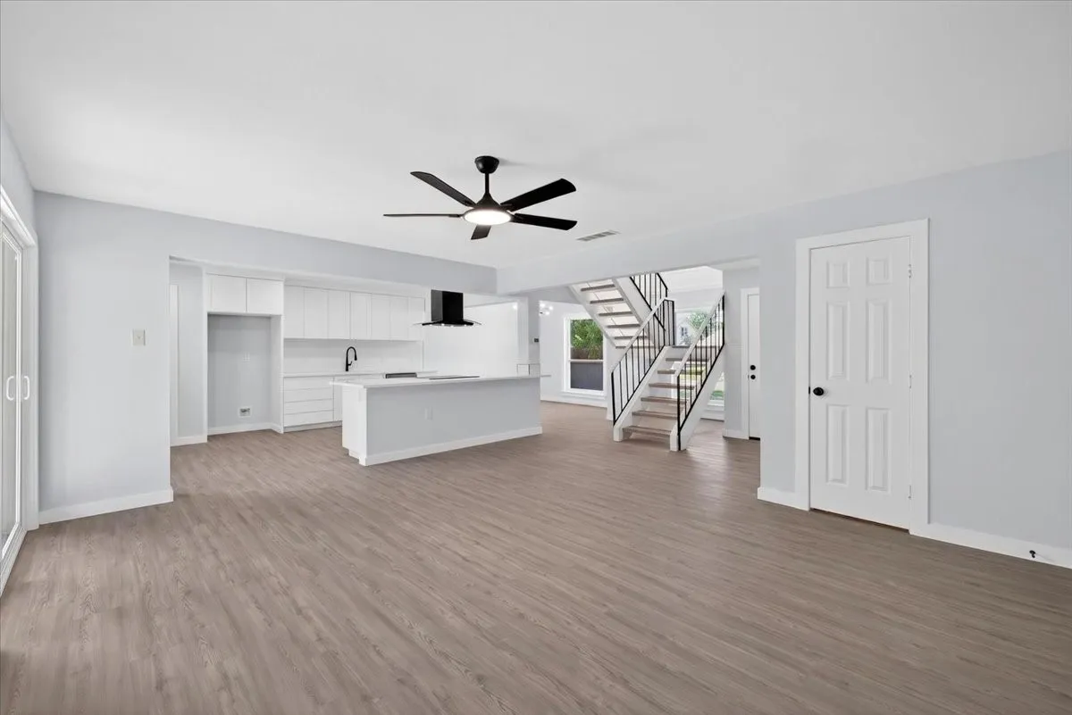 Spacious open concept living area featuring wood-finish flooring, a contemporary kitchen island, white cabinetry, and a modern black ceiling fan