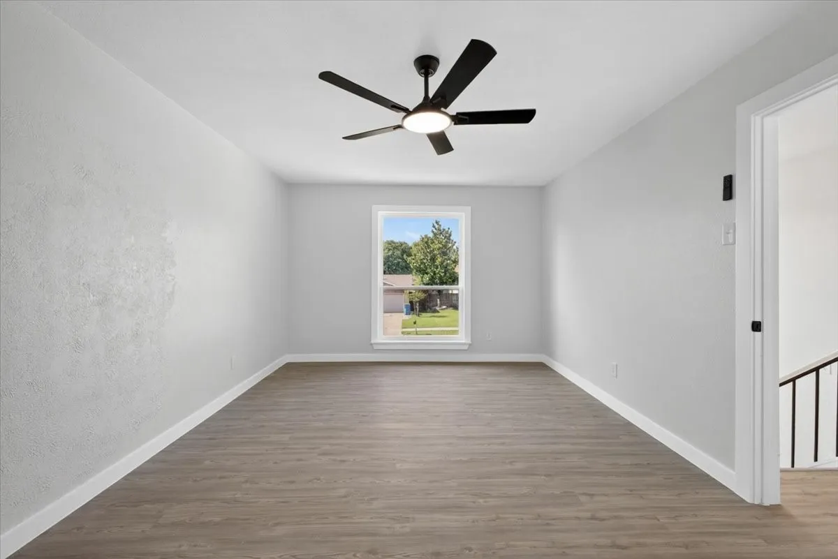 Spacious room featuring wood-finish flooring, a contemporary ceiling fan with integrated lighting, and crisp white baseboards