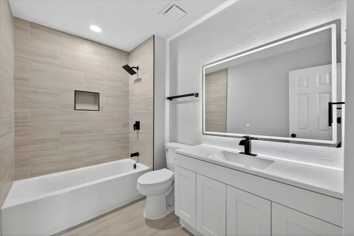Contemporary bathroom featuring a spacious vanity with white cabinetry, integrated sink, and an illuminated mirror