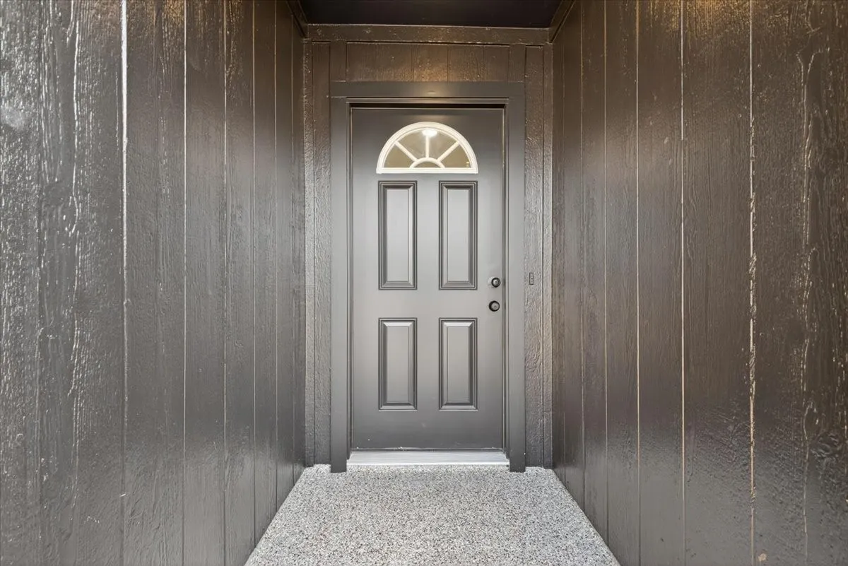 Entryway featuring a paneled door with a half-moon glass insert, textured vertical siding, and a speckled aggregate floor