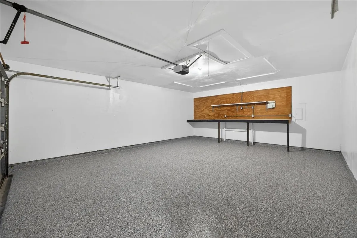 Spacious garage featuring a durable epoxy-coated concrete floor, white painted walls, built-in workbench with integrated lighting, and fluorescent overhead lighting
