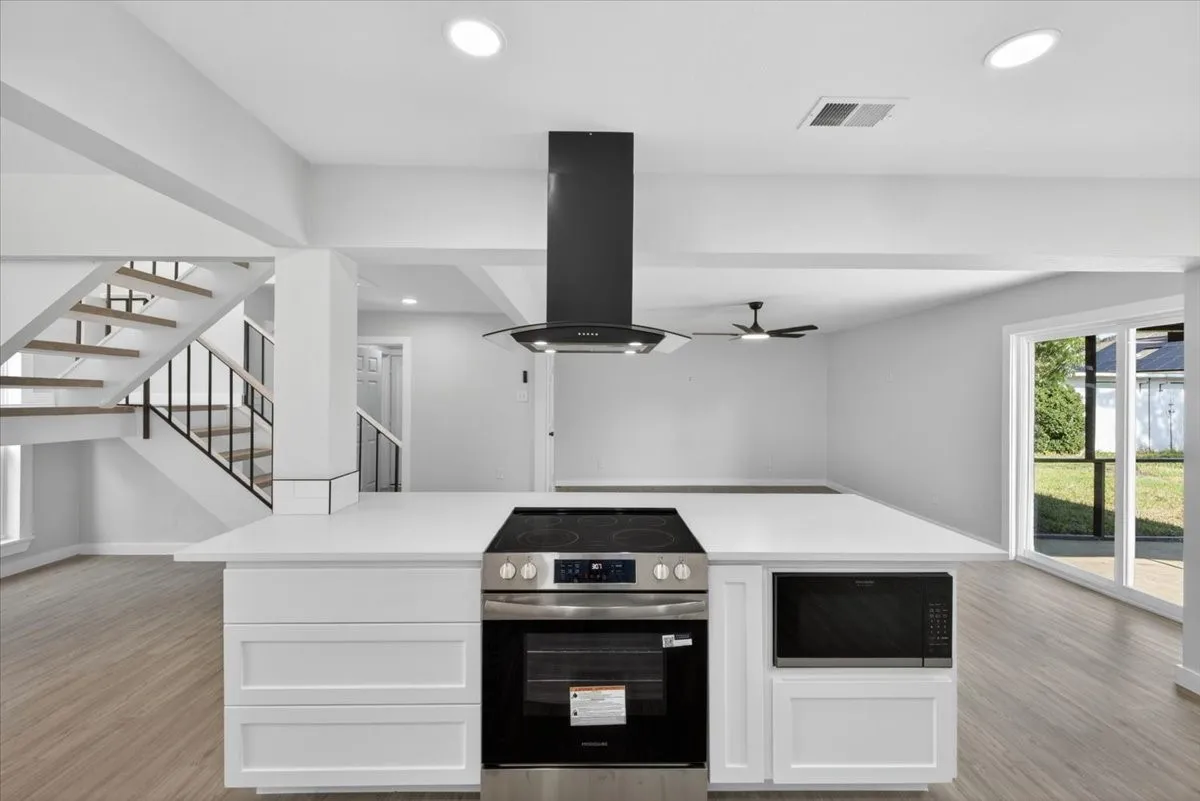 Kitchen island featuring a built-in stainless steel range, integrated microwave, and a contemporary black range hood