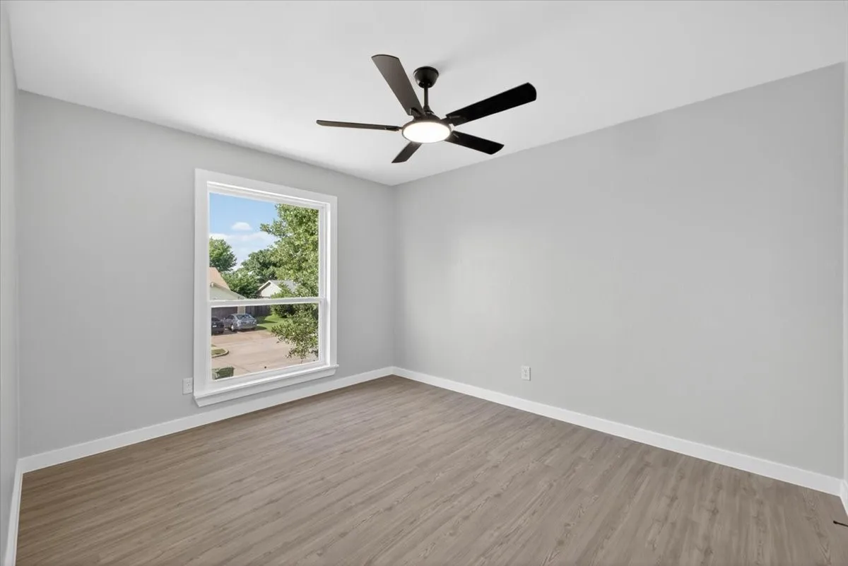 Neutral gray walls with white trim, wood-finish flooring, a contemporary ceiling fan with integrated lighting, and a double-hung window providing outdoor scenery