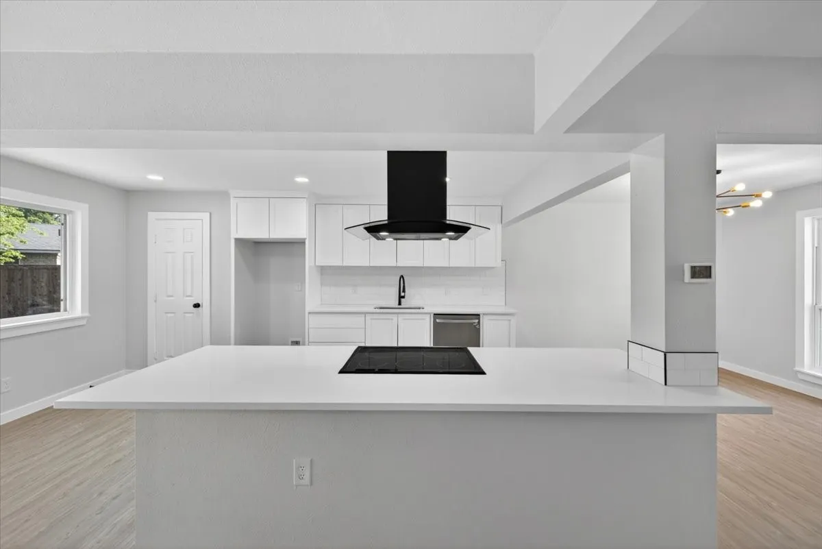 Modern kitchen featuring a large island with an integrated cooktop, white cabinetry, a black range hood, and subway tile backsplash