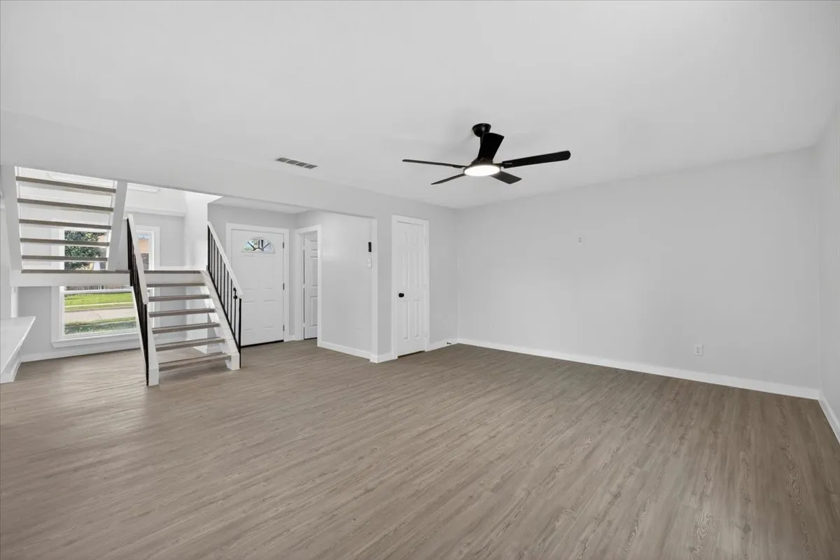 Spacious interior featuring wood-finish flooring, a contemporary ceiling fan with integrated lighting, and a two-story staircase with dark balusters