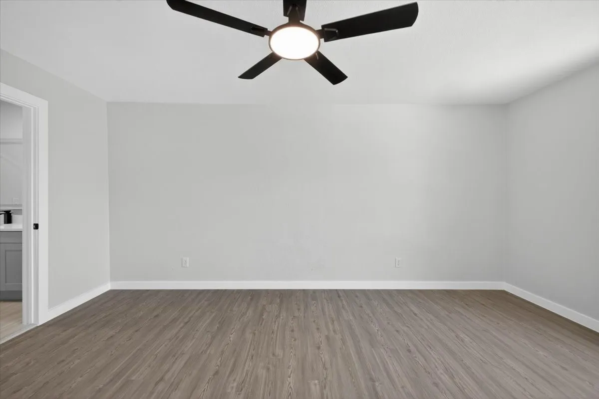 Spacious interior room featuring wood-finish flooring, white baseboards, and light gray wall paint