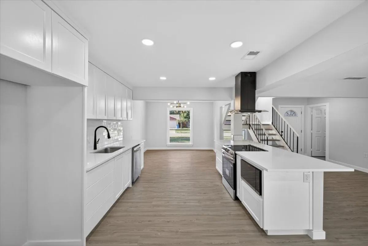 Modern kitchen featuring white cabinetry, light-toned countertops, stainless steel appliances, and wood-finish flooring