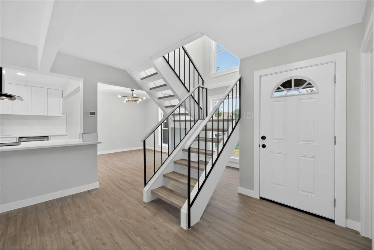 Inviting entryway featuring a white paneled front door with an arched decorative glass insert, wood-finish flooring, a contemporary staircase with black metal balusters and wood-finish treads, and a kitchen pass-through bar