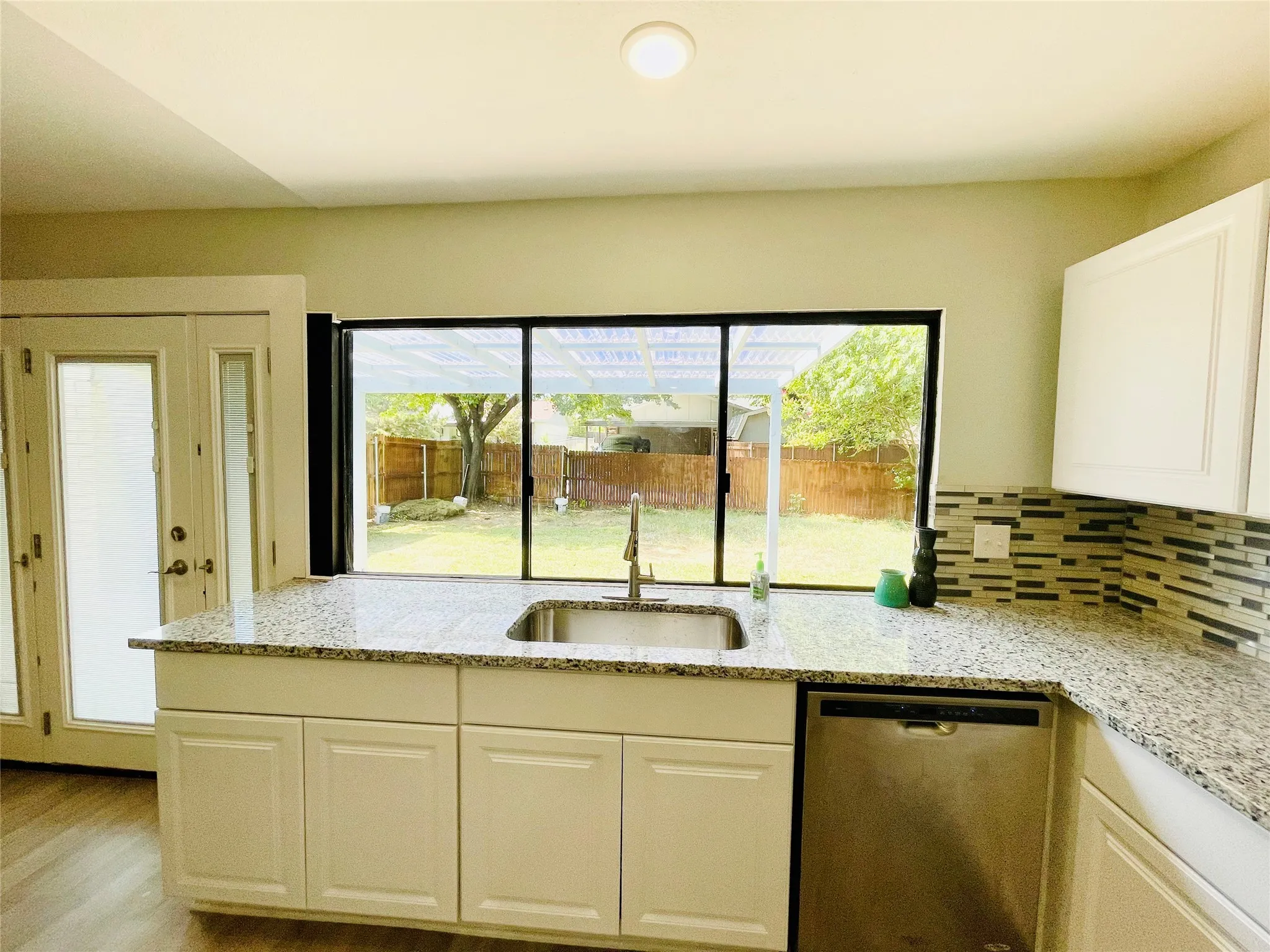 Kitchen featuring light wood-type flooring, sink, a wealth of natural light, tasteful backsplash, and stainless steel dishwasher