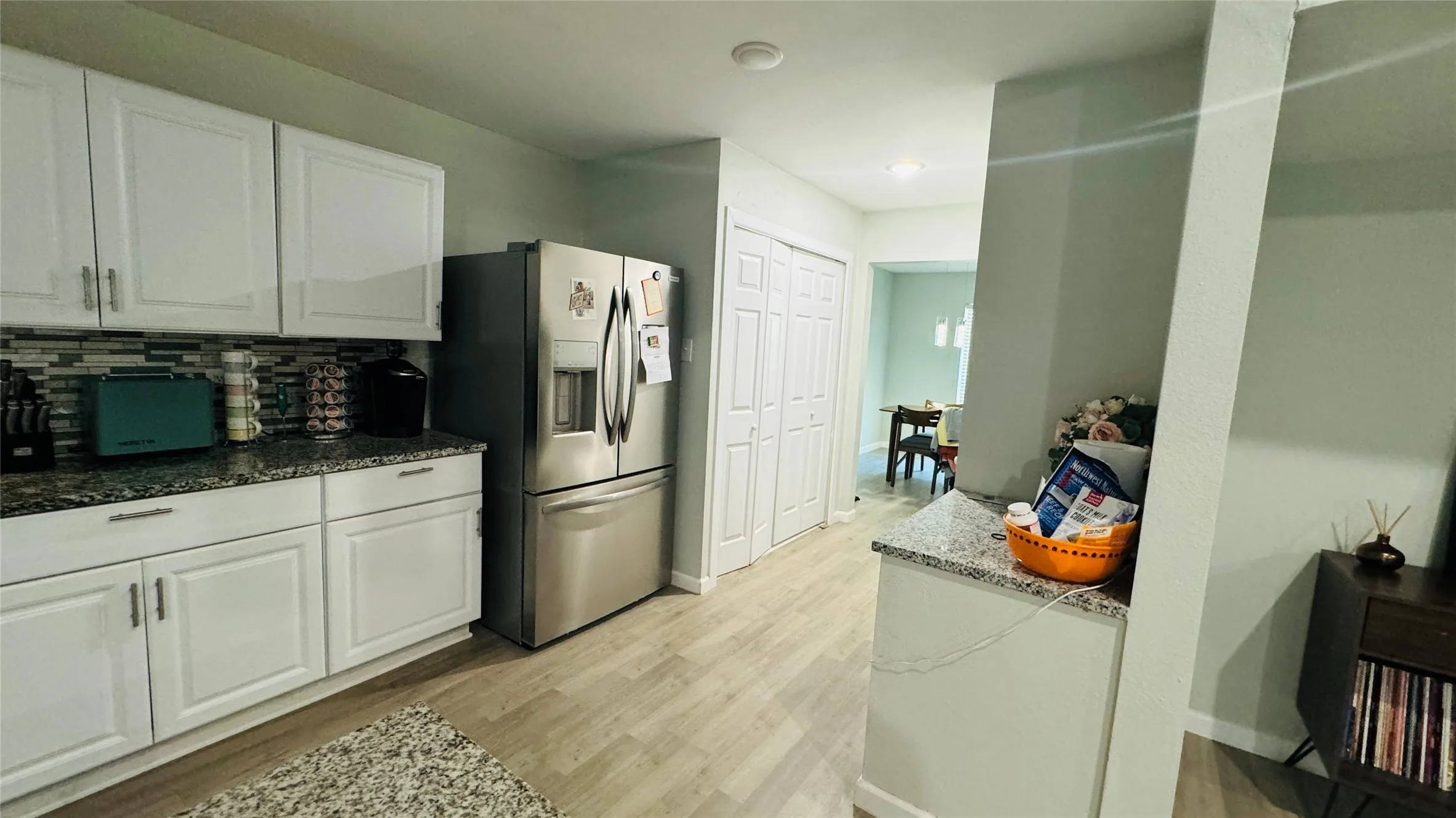 Kitchen featuring stainless steel fridge, tasteful backsplash, white cabinetry, light wood-type flooring, and dark stone counters