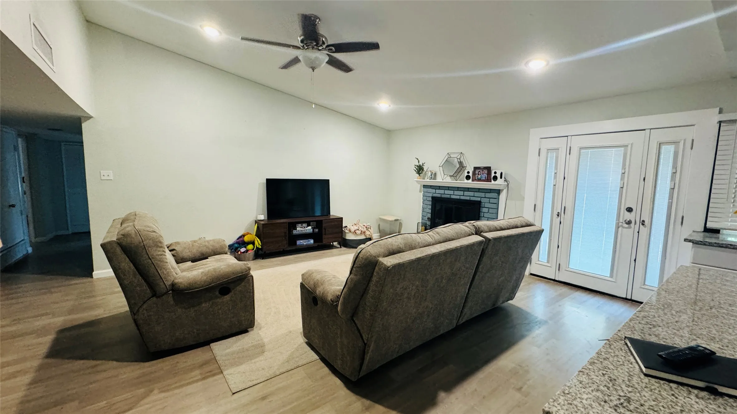Living room with lofted ceiling, ceiling fan, hardwood / wood-style floors, and a brick fireplace