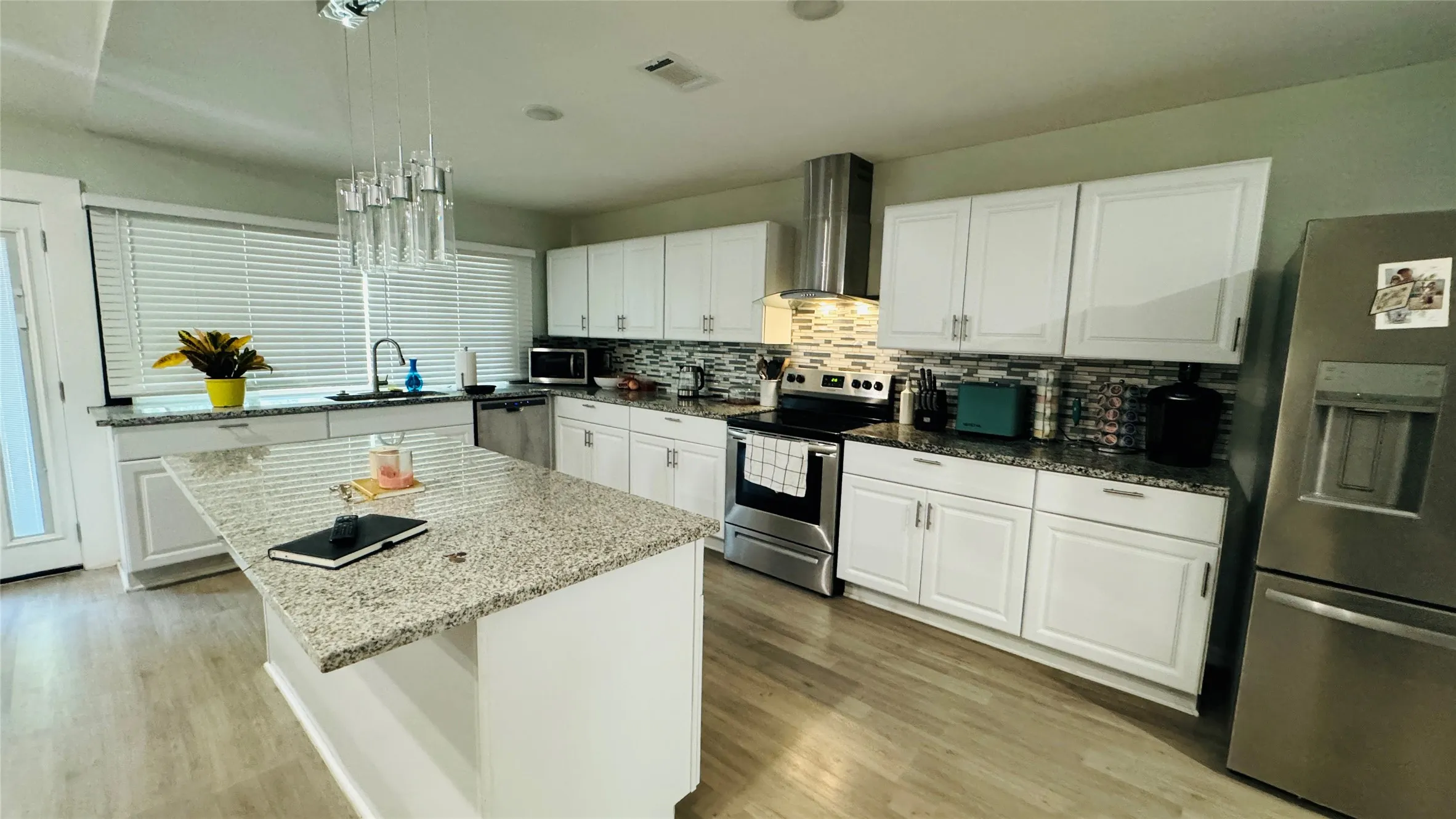 Kitchen with light hardwood / wood-style floors, a center island, stainless steel appliances, white cabinetry, and wall chimney range hood