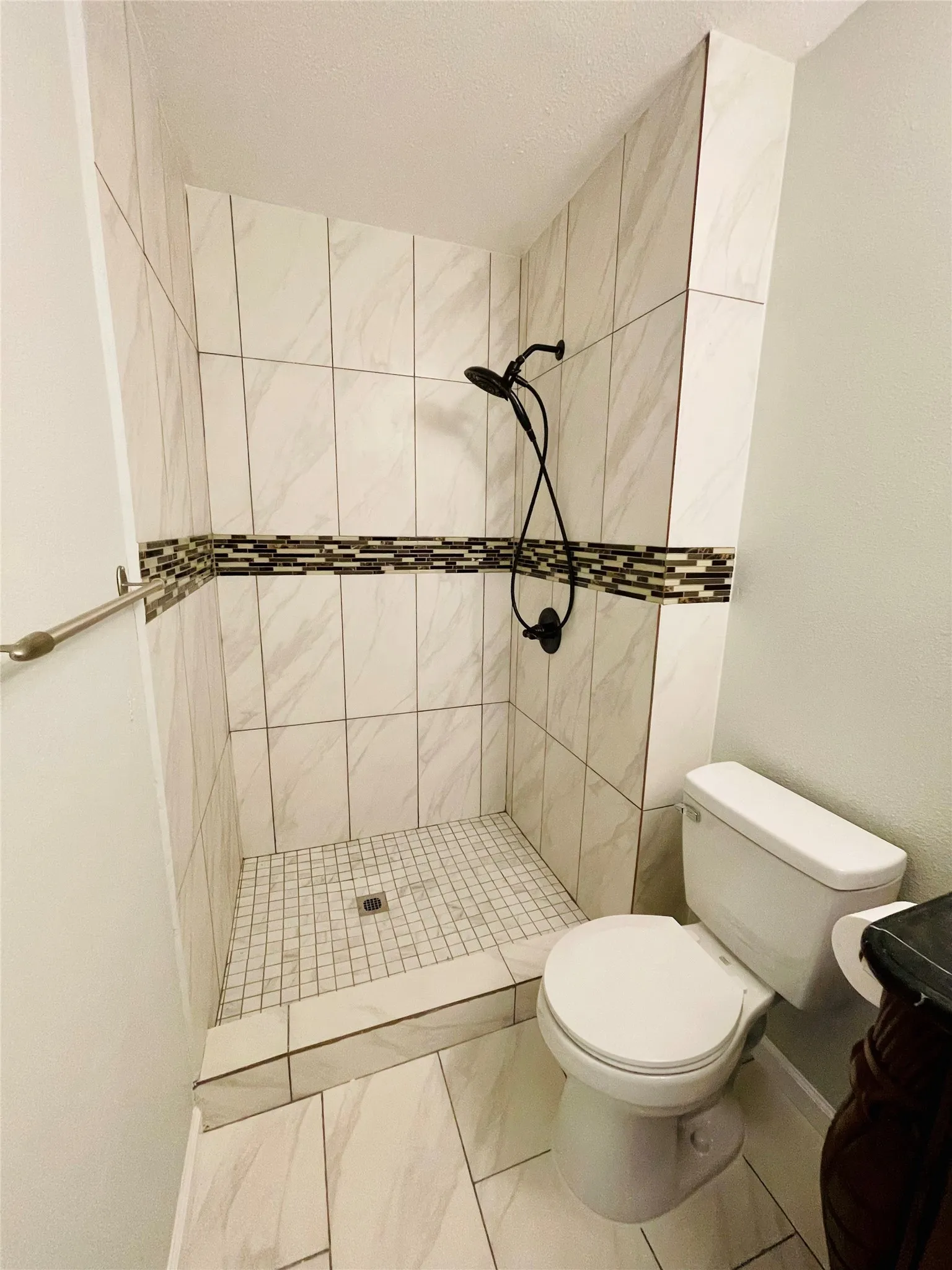 Bathroom with toilet, a tile shower, and tile patterned floors