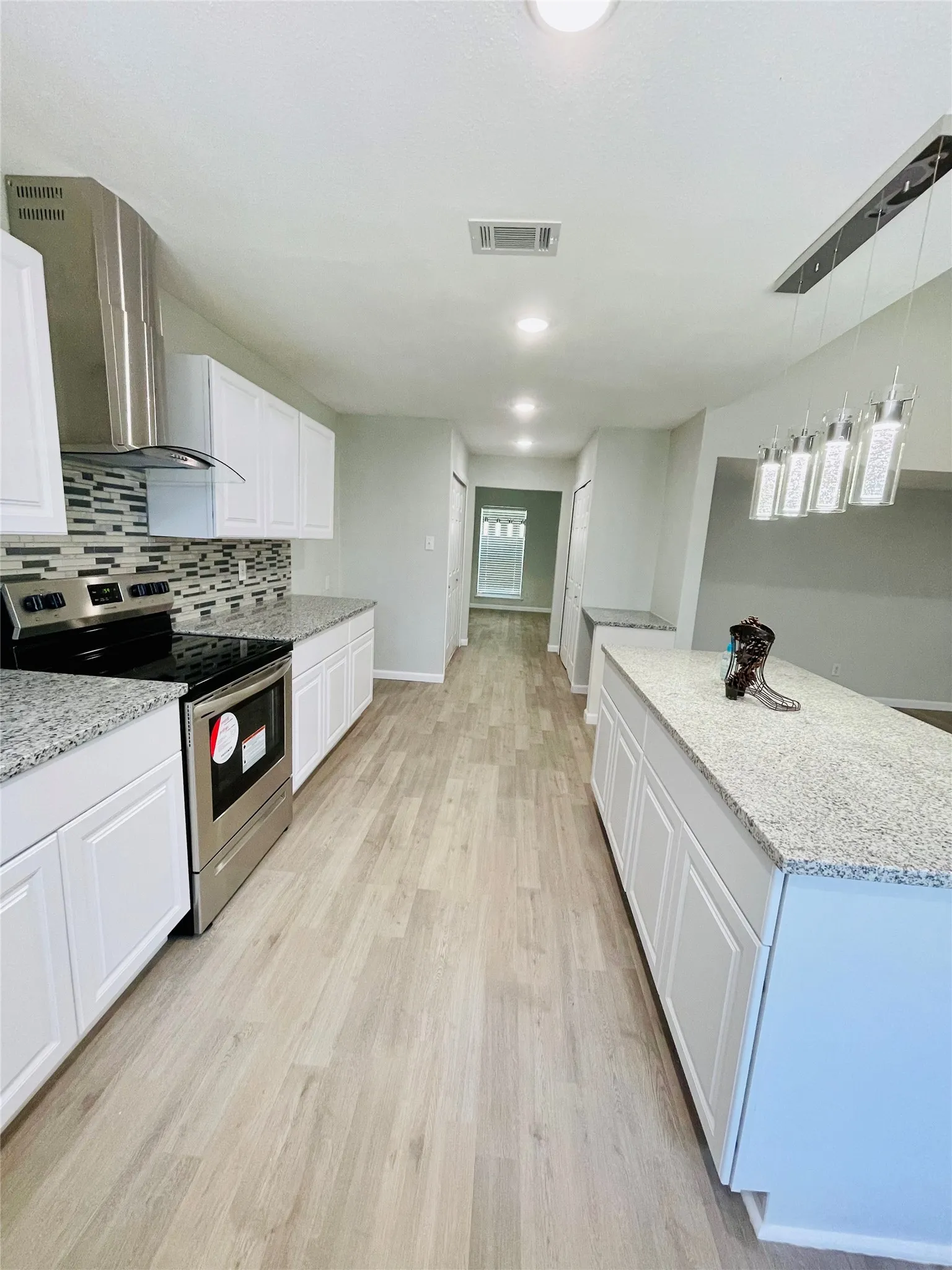 Kitchen featuring stainless steel electric stove, decorative light fixtures, light hardwood / wood-style flooring, light stone counters, and wall chimney range hood