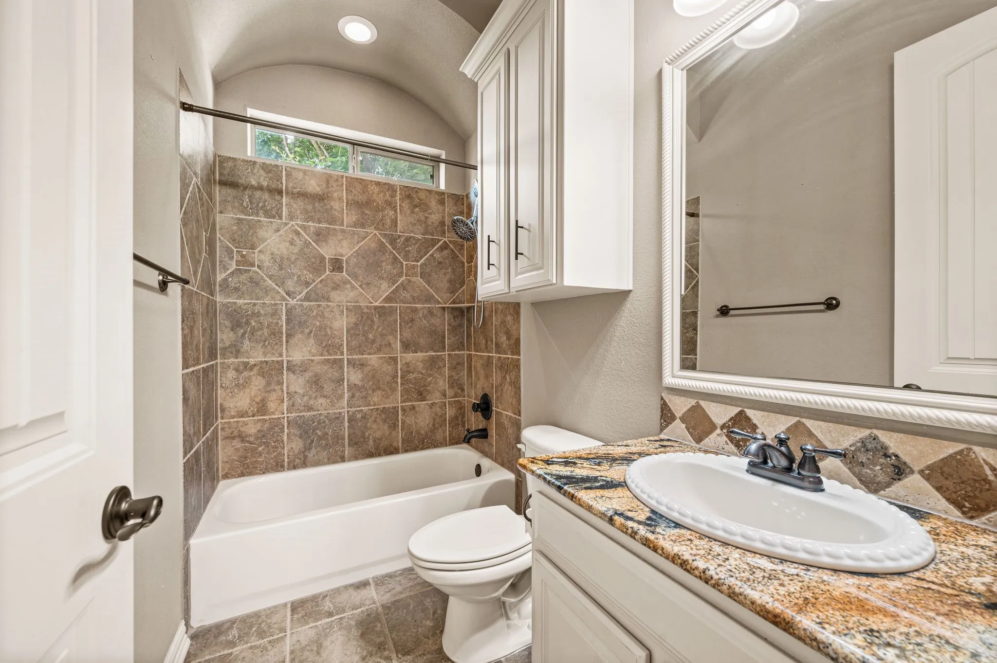 A secondary bath located between bedrooms downstairs includes a linen cabinet, tile flooring, tile surround tub with rain shower head, granite topped vanity, decorative oval sink, elongated toilet, bronze fixtures and hardware and a framed mirror.
