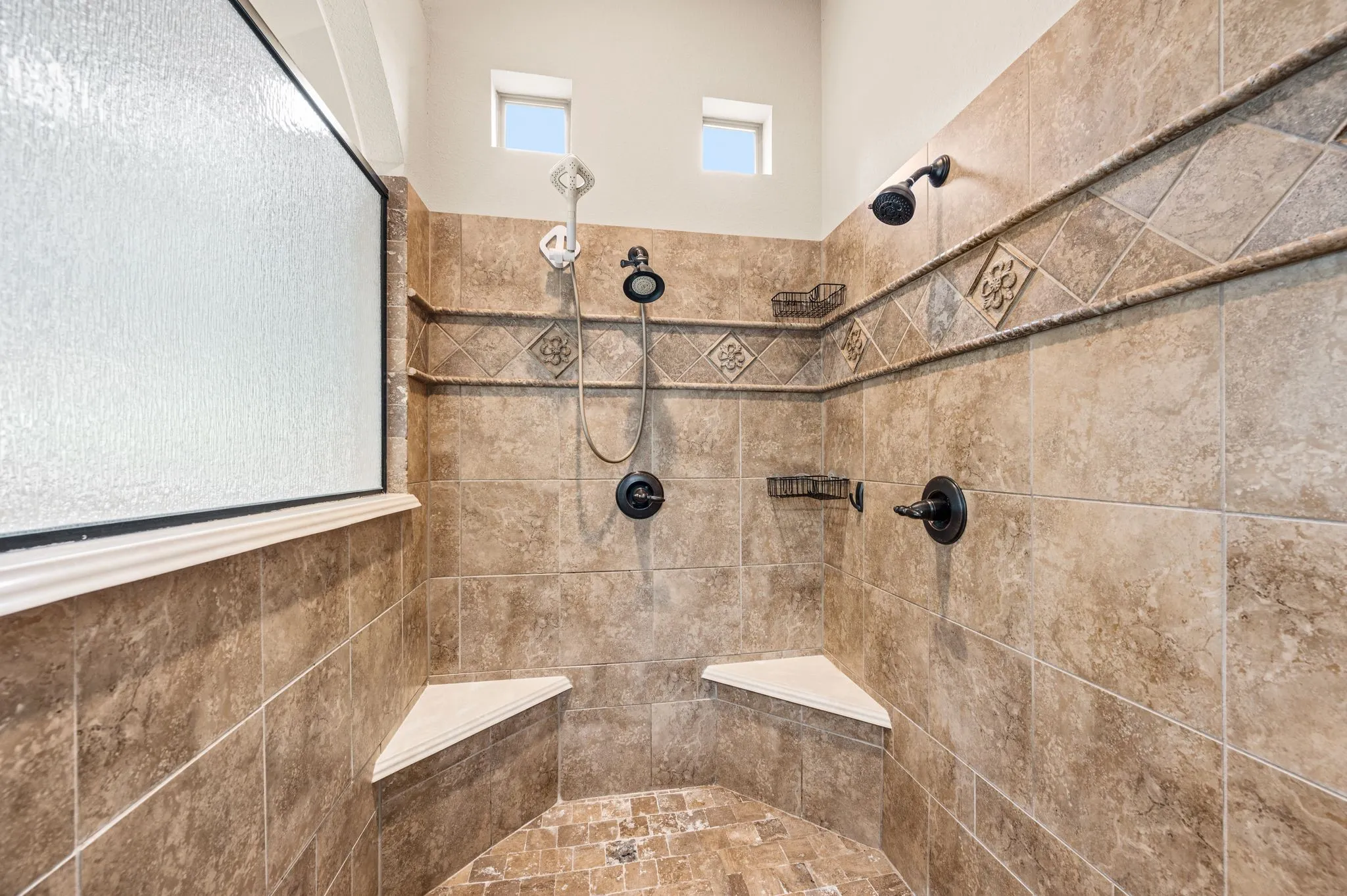 The fully tiled Primary shower includes bench seats, and bronze fixtures with dual body sprays.