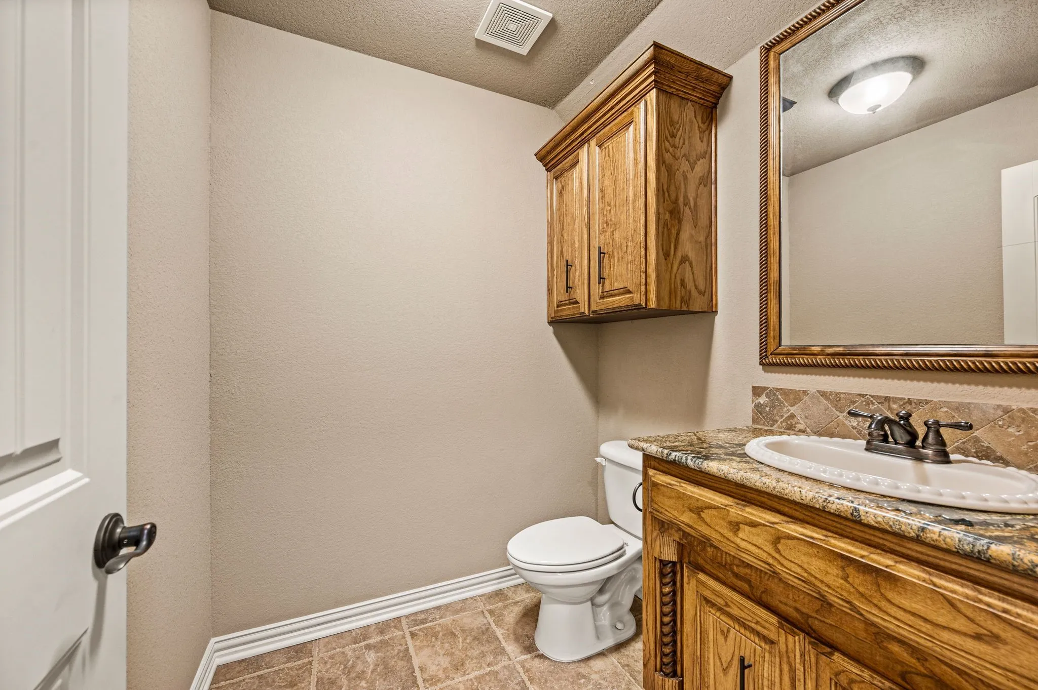 A half bath with linen cabinet, tile flooring, vanity with granite counter and oval sink, framed mirror and bronze fixtures and hardware is located upstairs next to the bonus room.