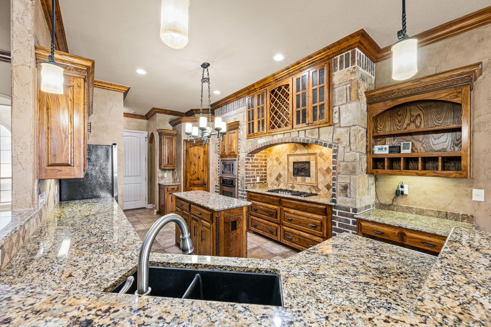 Brick and stone frame the 5 burner gas cook top. Glass front cabinets and wine storage compliment the space. Multiple drawers allow for easy access to pots and pans. Built in desk. Walk in pantry.