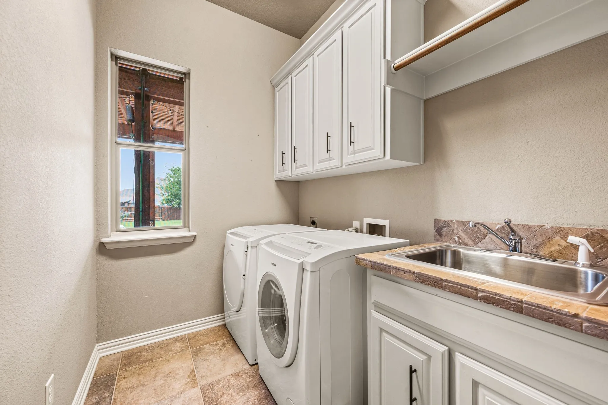 The spacious laundry room provides ample storage cabinetry, a vanity sink and hanging clothes rack. The washer and dryer are included.