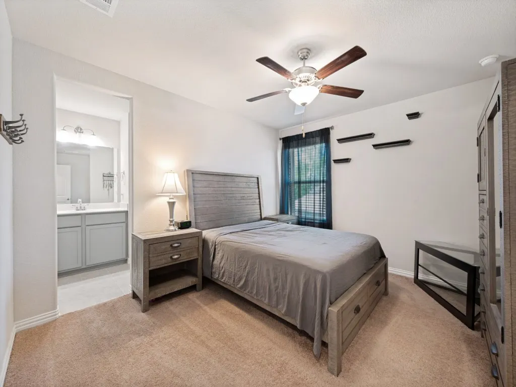 Carpeted sleeping area featuring a wood-finish bed frame with an integrated headboard and a ceiling fan with light fixture