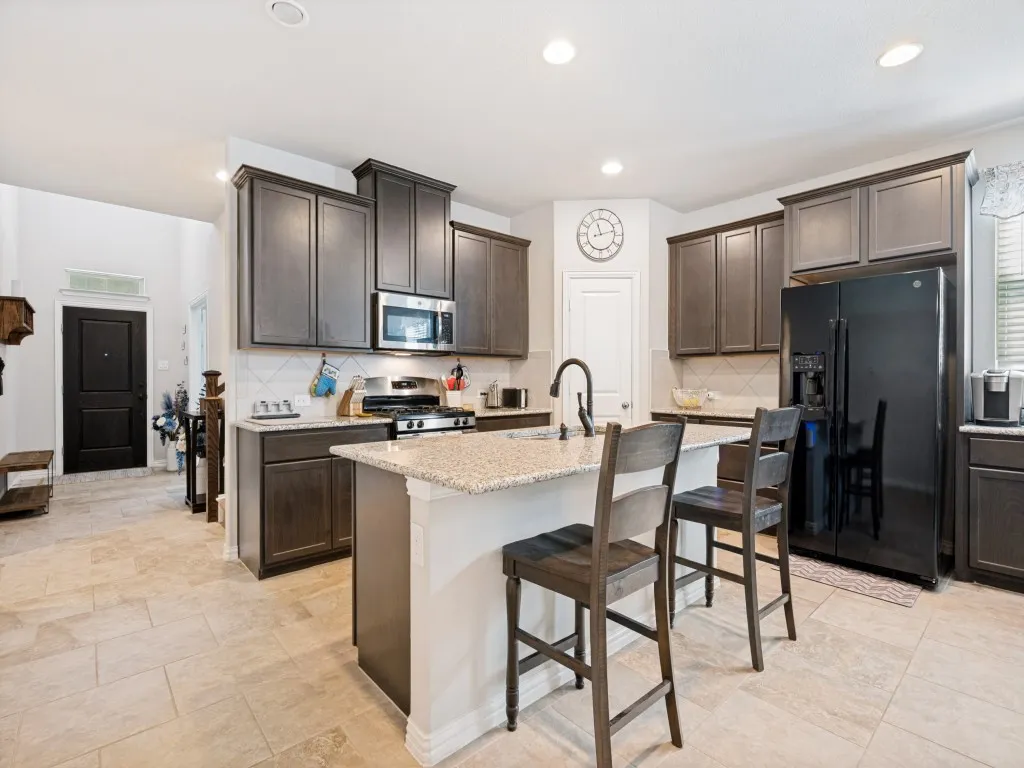 Kitchen featuring an island with granite countertop, dark wood-finish cabinetry, stainless steel microwave, gas range, and large format tile flooring