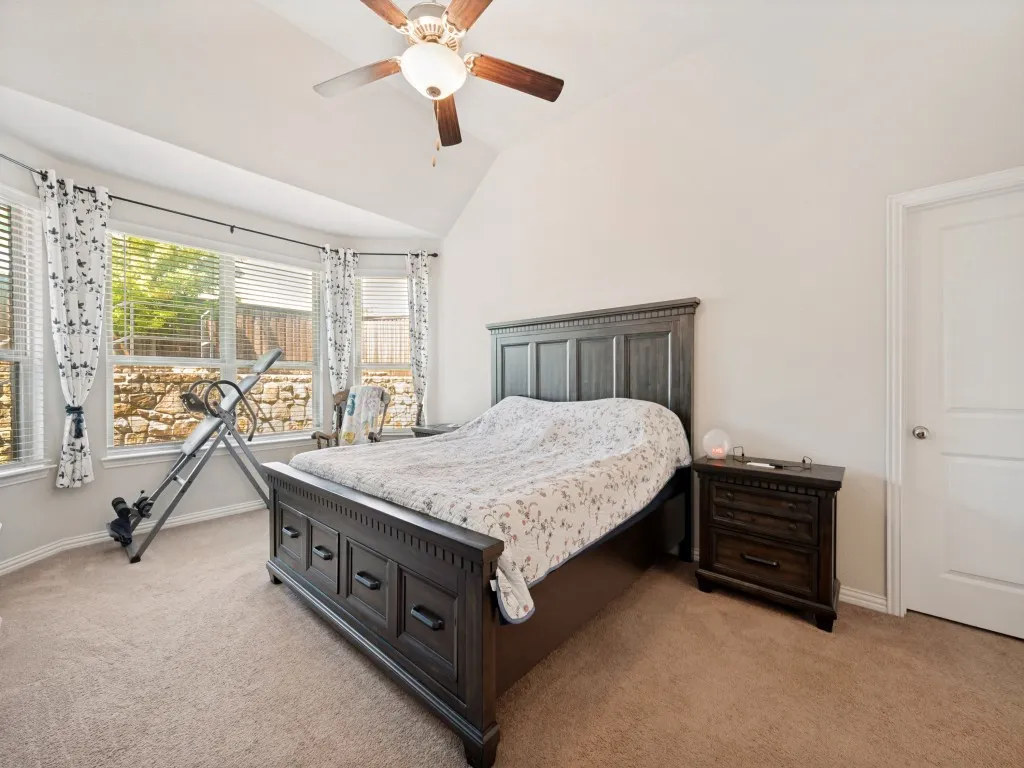 Vaulted ceiling bedroom with a bay window, ceiling fan, carpet flooring, and a stone wall exterior