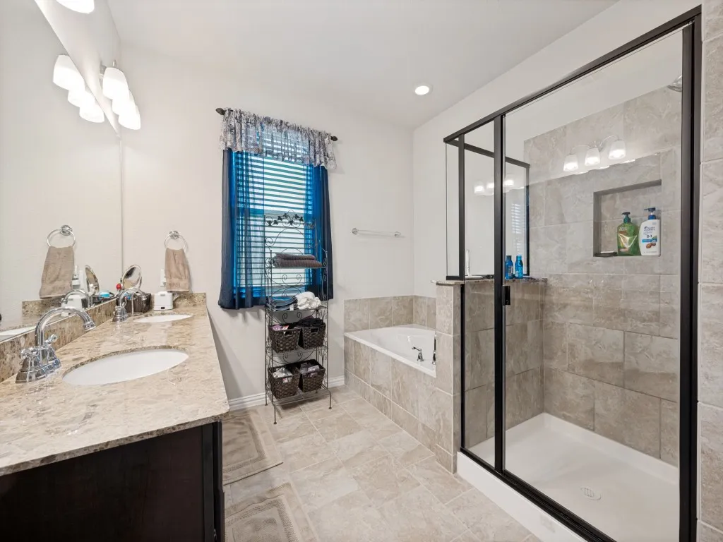 Bathroom featuring a dual vanity with stone countertops, a soaking tub, and a glass-enclosed shower with tiled walls and a recessed niche