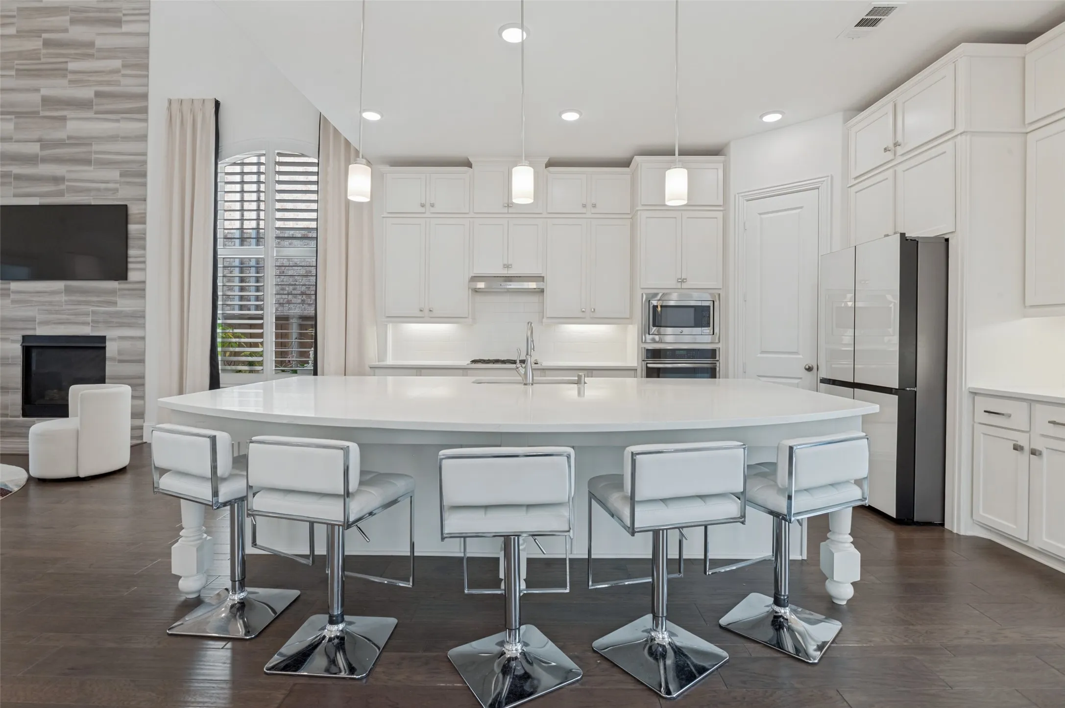Spacious kitchen with a large curved island, white cabinetry, dark wood-finish flooring, recessed lighting, and stainless steel appliances