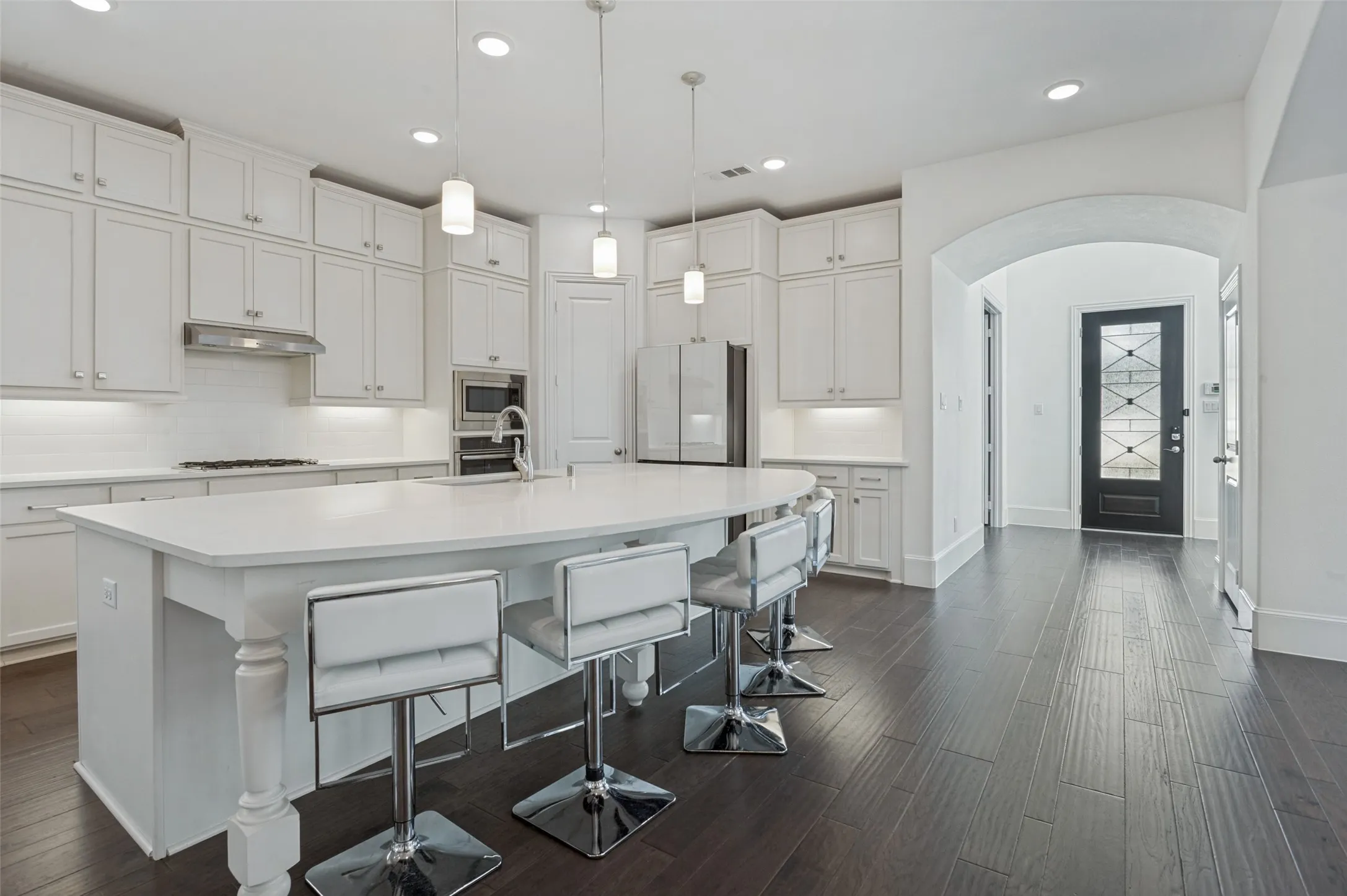 Contemporary kitchen featuring white cabinetry, a large central island with seating, stainless steel appliances, and dark wood-finish flooring