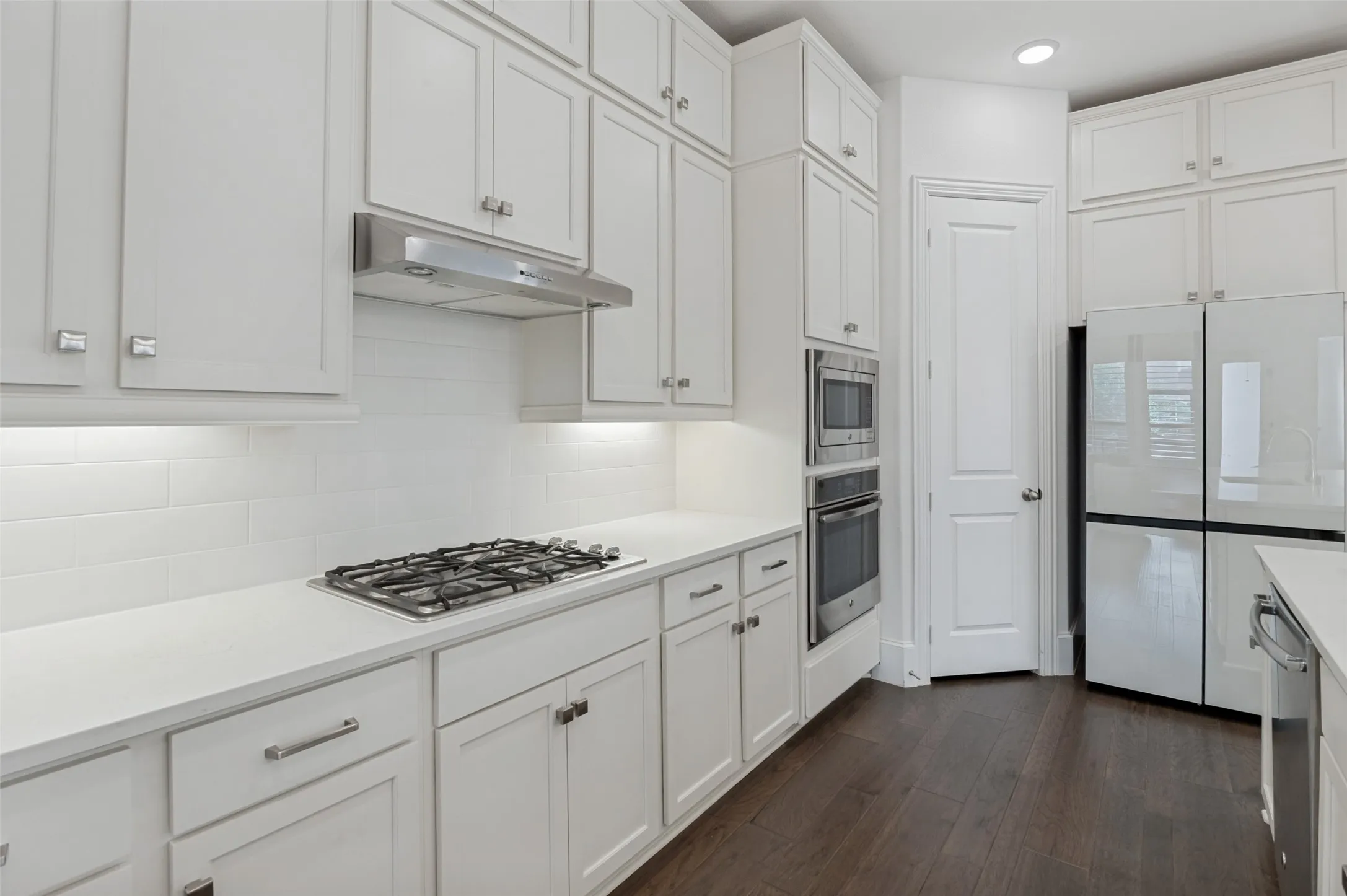 Kitchen featuring white shaker-style cabinetry, stainless steel appliances including a gas cooktop, built-in double oven, and refrigerator, white subway tile backsplash, and dark wood-finish flooring