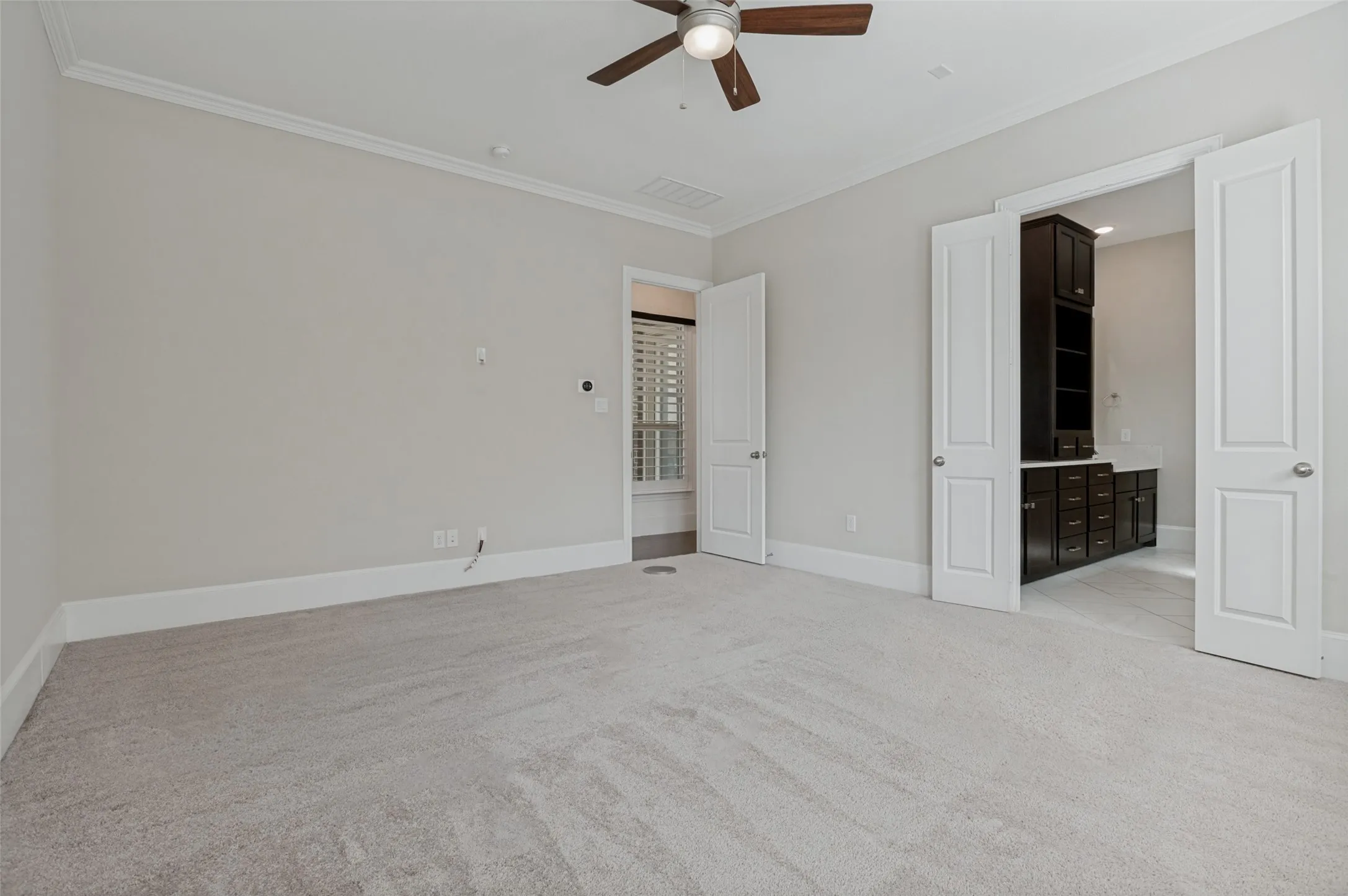 Spacious carpeted room featuring a ceiling fan with wood-finish blades, white trim, and crown molding
