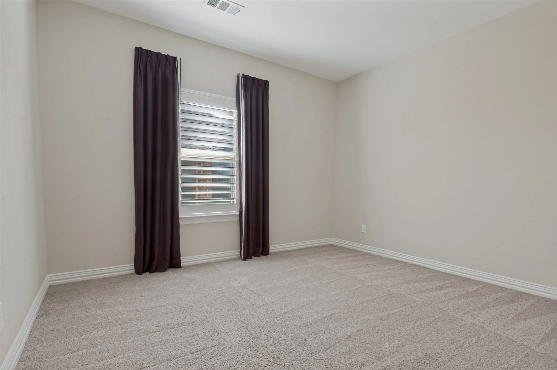 Neutral-toned room featuring a single window with white plantation shutters