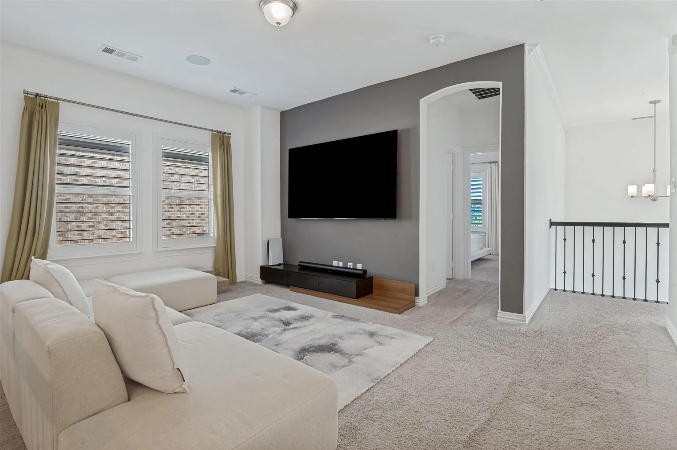 Carpeted media room featuring a large wall-mounted television, a built-in floating console, and dual windows with blinds and curtains